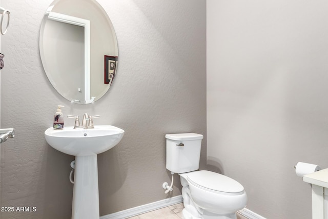 half bathroom with a textured wall, tile patterned flooring, toilet, and baseboards