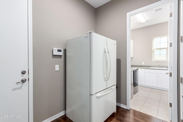 kitchen featuring wood finished floors, freestanding refrigerator, light countertops, white cabinetry, and a sink