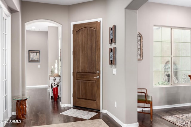 entrance foyer with arched walkways, a healthy amount of sunlight, dark wood-style flooring, and baseboards