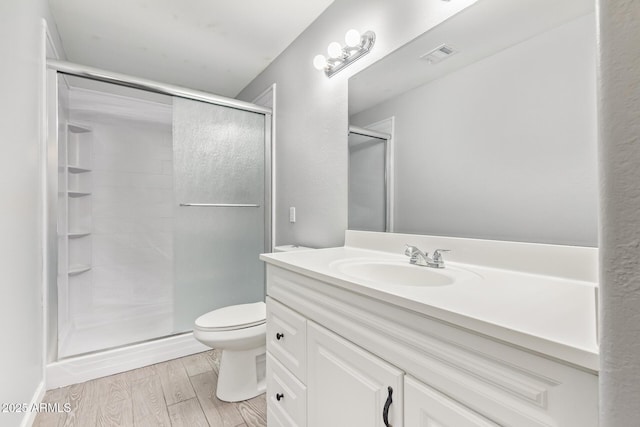 bathroom with wood-type flooring, toilet, a shower with shower door, and vanity