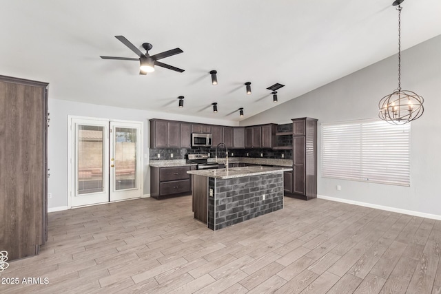 kitchen featuring lofted ceiling, appliances with stainless steel finishes, dark brown cabinetry, a center island with sink, and decorative light fixtures