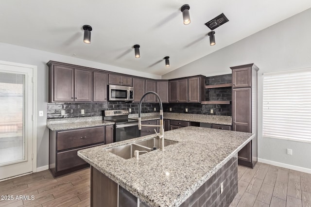 kitchen with a kitchen island with sink, dark brown cabinets, vaulted ceiling, and appliances with stainless steel finishes