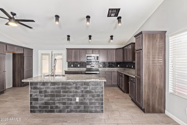 kitchen featuring lofted ceiling, sink, dark brown cabinets, a center island with sink, and stainless steel appliances