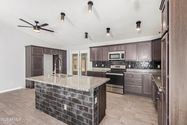 kitchen featuring sink, appliances with stainless steel finishes, a kitchen island with sink, dark brown cabinets, and light stone counters