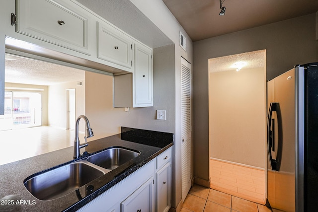 kitchen featuring sink, light tile patterned floors, stainless steel fridge, white cabinets, and dark stone counters