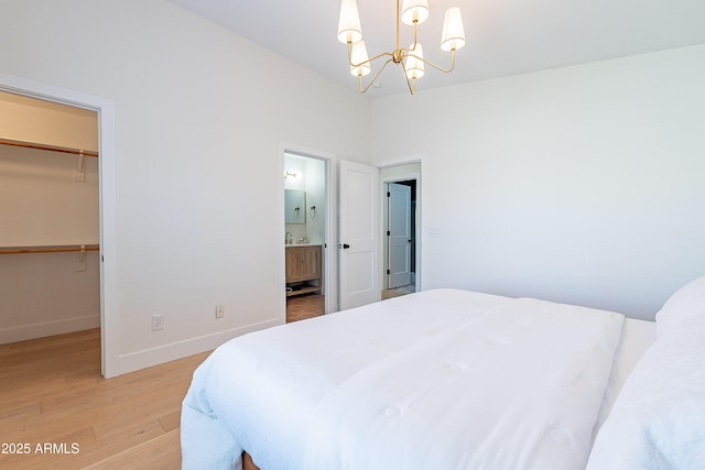 bedroom with a spacious closet, hardwood / wood-style floors, a closet, an inviting chandelier, and connected bathroom