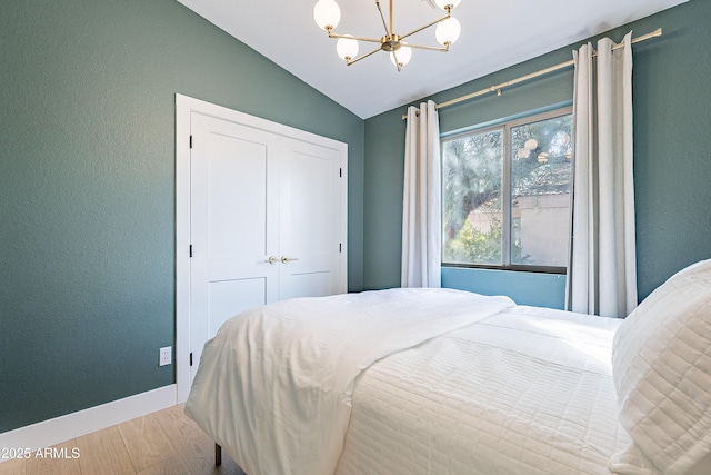 bedroom featuring a closet, vaulted ceiling, a notable chandelier, and light wood-type flooring