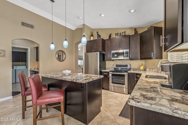 kitchen featuring decorative light fixtures, a center island, sink, washing machine and clothes dryer, and appliances with stainless steel finishes