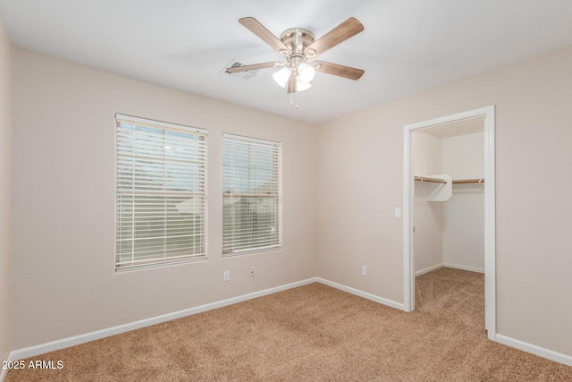 unfurnished bedroom with a ceiling fan, baseboards, a closet, a walk in closet, and light colored carpet