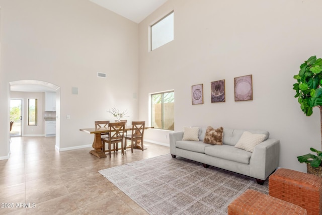 living area with visible vents, baseboards, light tile patterned floors, a towering ceiling, and arched walkways