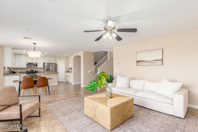 living room featuring visible vents, arched walkways, baseboards, ceiling fan, and stairs