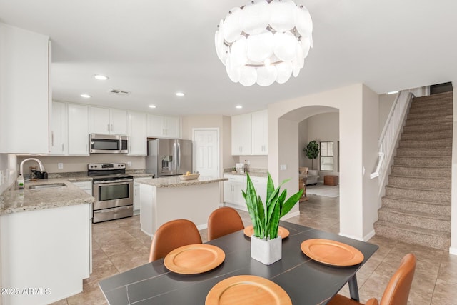 kitchen with a sink, arched walkways, appliances with stainless steel finishes, white cabinets, and a chandelier