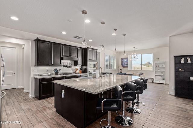 kitchen with appliances with stainless steel finishes, pendant lighting, a kitchen bar, light hardwood / wood-style flooring, and a kitchen island with sink