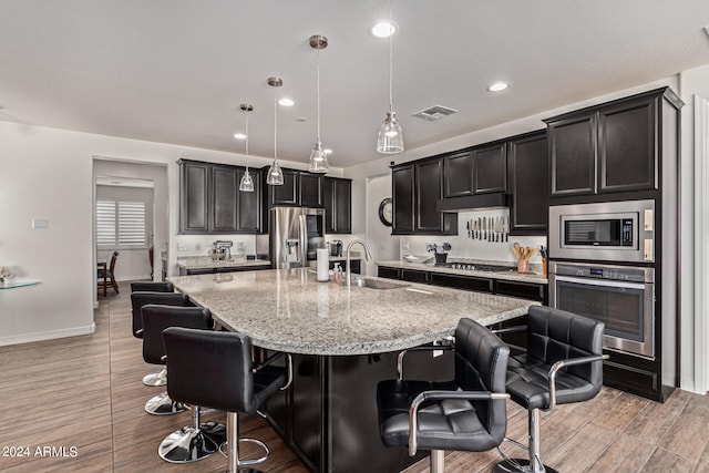 kitchen featuring light hardwood / wood-style flooring, a kitchen breakfast bar, a center island with sink, appliances with stainless steel finishes, and decorative light fixtures