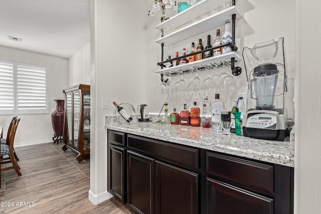 bar featuring light stone countertops, dark brown cabinetry, and hardwood / wood-style floors