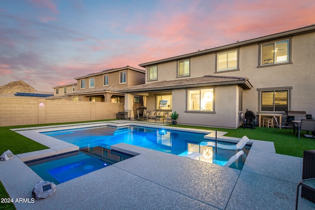 pool at dusk with a lawn, an in ground hot tub, and a patio area