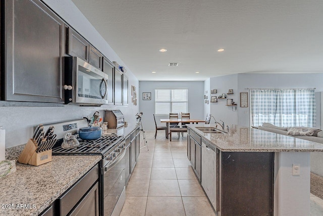 kitchen with stainless steel appliances, sink, a kitchen island with sink, light stone counters, and light tile patterned floors