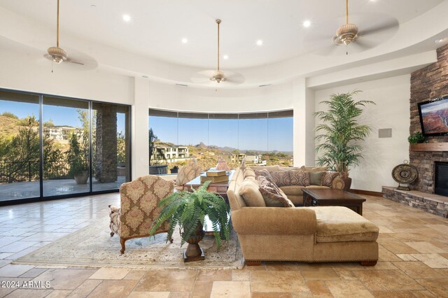 tiled living room featuring plenty of natural light, ceiling fan, a raised ceiling, and a fireplace