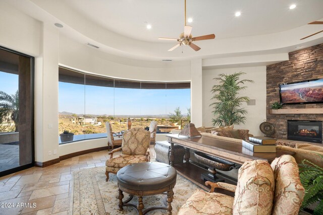 living room featuring stone tile flooring, a healthy amount of sunlight, a fireplace, and ceiling fan