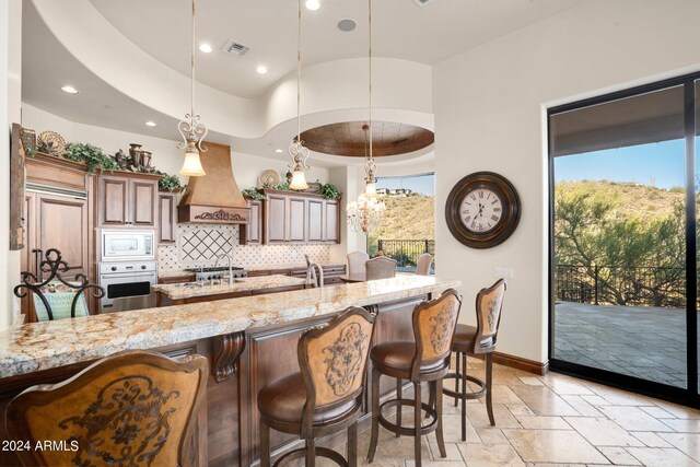 kitchen featuring stone tile floors, light stone countertops, white microwave, custom range hood, and stainless steel oven