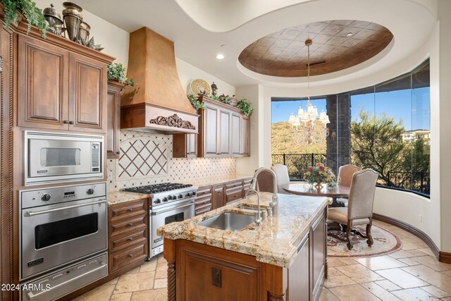 kitchen featuring premium range hood, appliances with stainless steel finishes, stone tile flooring, a raised ceiling, and a sink