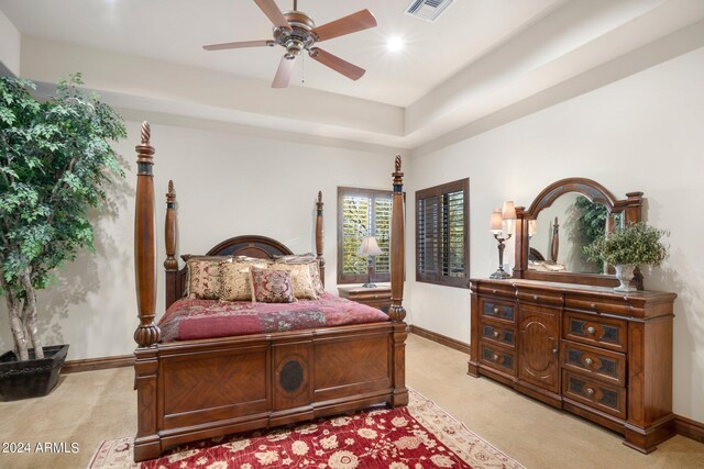 bedroom with visible vents, baseboards, a tray ceiling, light carpet, and a ceiling fan