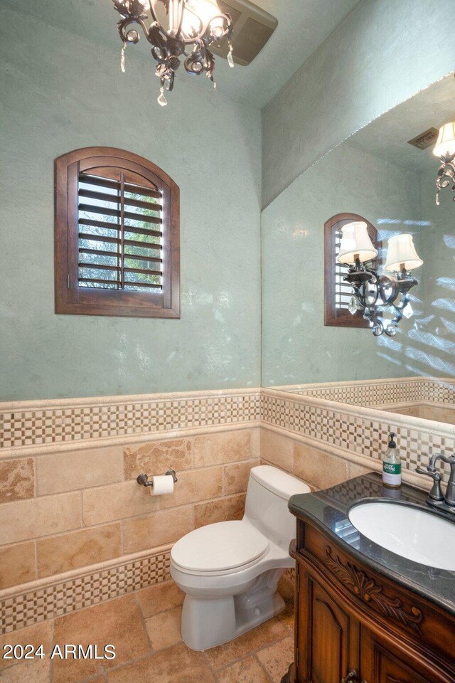 bathroom with tile floors, vanity, tile walls, a chandelier, and toilet