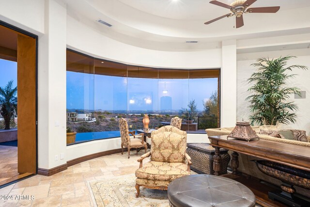 living area featuring a raised ceiling, ceiling fan, and light tile floors