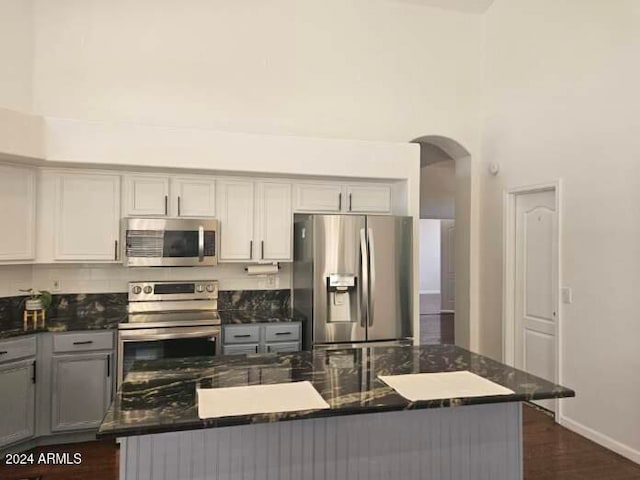 kitchen featuring gray cabinetry, a towering ceiling, dark wood-type flooring, and appliances with stainless steel finishes