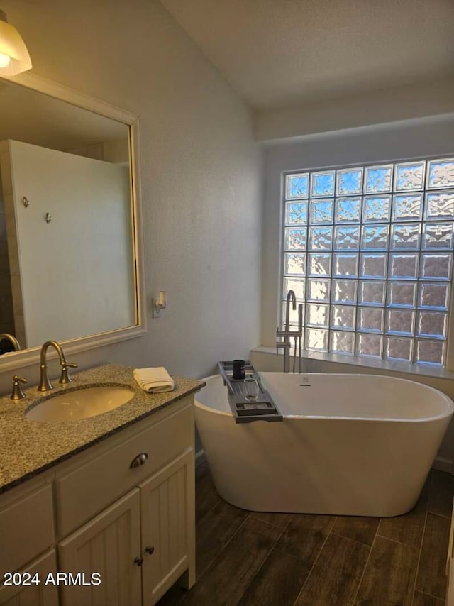 bathroom featuring vanity, wood-type flooring, lofted ceiling, and a tub