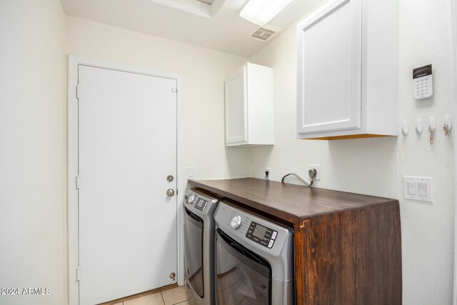 clothes washing area featuring cabinets, light tile patterned floors, and washing machine and clothes dryer