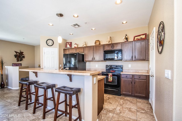 kitchen featuring a kitchen breakfast bar, an island with sink, dark brown cabinets, black appliances, and pendant lighting