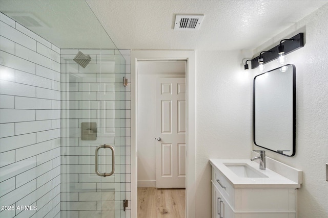 full bath featuring a shower stall, a textured ceiling, wood finished floors, and vanity