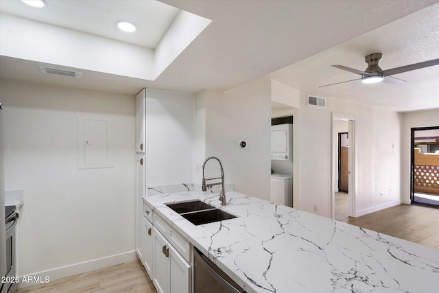 kitchen with estacked washer and dryer, a sink, light wood-style flooring, white cabinetry, and light stone countertops