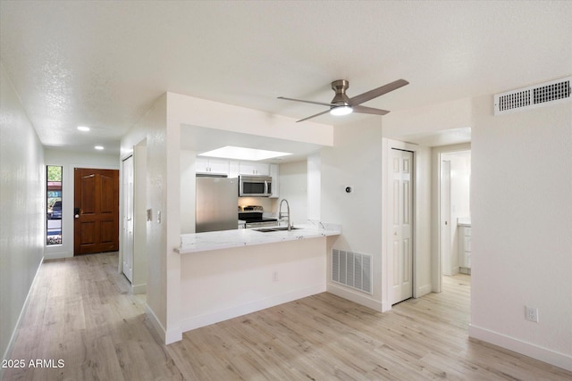 kitchen with stainless steel appliances, a sink, light wood-type flooring, light countertops, and a textured ceiling