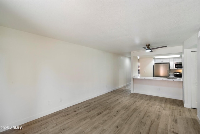 unfurnished living room with light wood finished floors, baseboards, and a textured ceiling