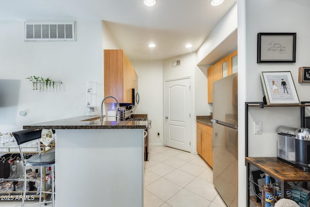 kitchen with kitchen peninsula, sink, light tile patterned floors, a kitchen bar, and stainless steel appliances