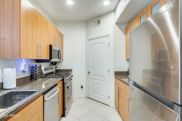 kitchen featuring light tile patterned floors, stainless steel appliances, and dark stone countertops