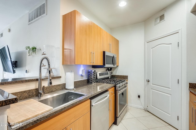 kitchen with sink, stainless steel appliances, dark stone counters, and light tile patterned floors