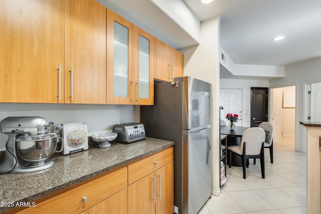 kitchen with light tile patterned floors, stainless steel fridge, and dark stone counters