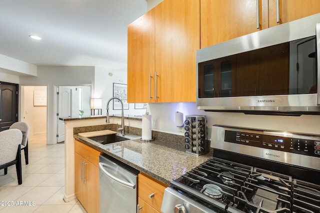 kitchen featuring sink, dark stone countertops, light tile patterned floors, and appliances with stainless steel finishes