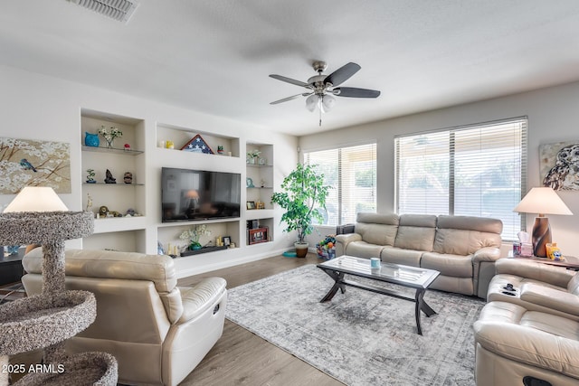 living room with ceiling fan, wood finished floors, visible vents, baseboards, and built in features