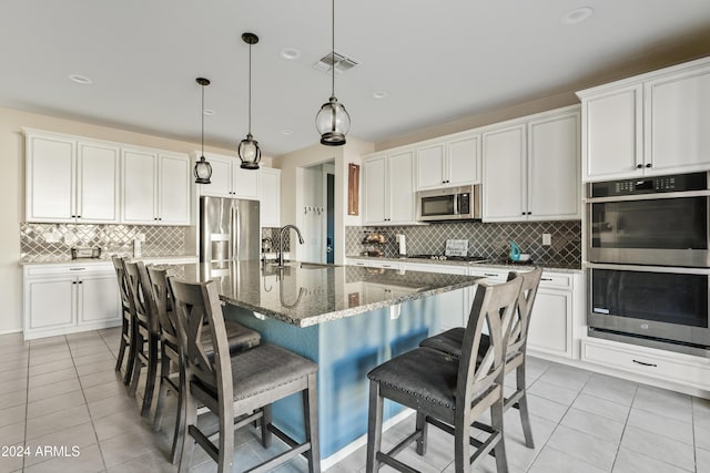 kitchen with light tile patterned flooring, an island with sink, white cabinets, and appliances with stainless steel finishes