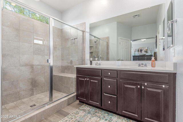 full bath featuring a sink, double vanity, a shower stall, wood finished floors, and visible vents
