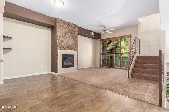 unfurnished living room featuring visible vents, a ceiling fan, a tile fireplace, wood finished floors, and stairs