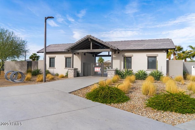view of front facade with a tiled roof, stucco siding, fence, a gate, and driveway