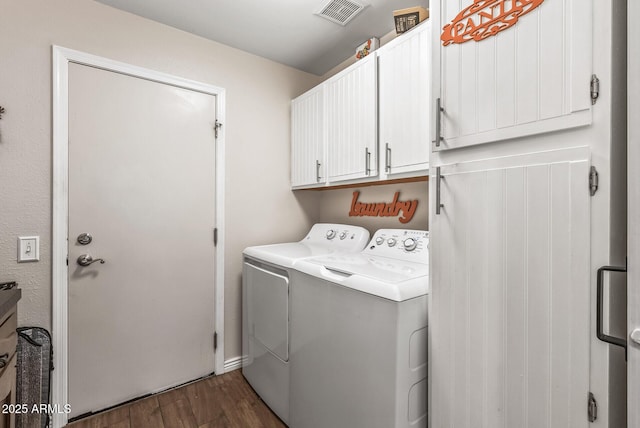 washroom featuring dark wood finished floors, cabinet space, washer and clothes dryer, and visible vents