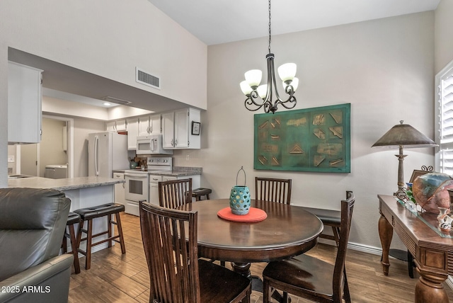 dining area with a towering ceiling, visible vents, a chandelier, wood finished floors, and washer / dryer