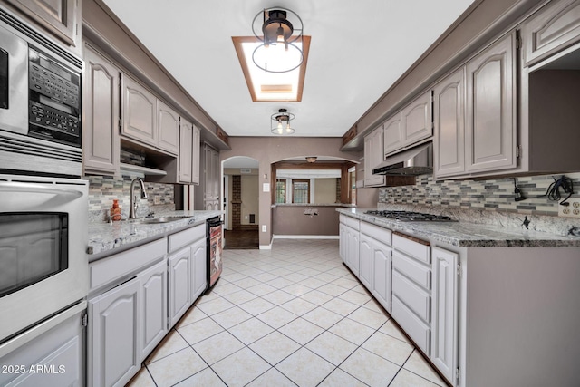 6217 W Orange Dr, Glendale, AZ 85301 - kitchen featuring arched walkways, under cabinet range hood, built in microwave, stainless steel gas stovetop, and backsplash