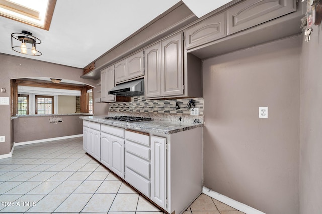 6217 W Orange Dr, Glendale, AZ 85301 - kitchen with under cabinet range hood, stainless steel gas stovetop, decorative backsplash, light tile patterned flooring, and arched walkways